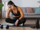 Mulher sentada no tapete de exercícios demonstrando cansaço após treino em casa feminino na sala