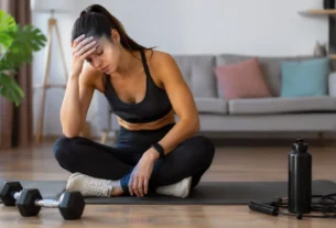 Mulher sentada no tapete de exercícios demonstrando cansaço após treino em casa feminino na sala