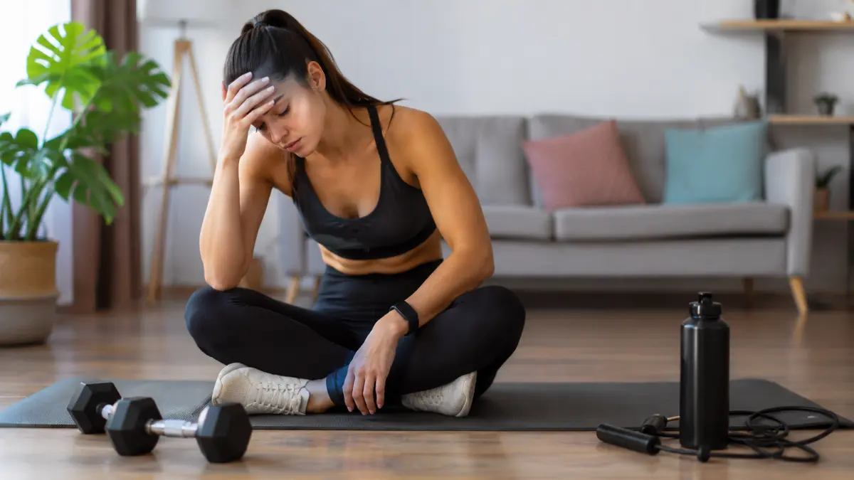 Erros no Treino em Casa Feminino: 11 Falhas que Travam Resultados 1 Mulher sentada no tapete de exercícios demonstrando cansaço após treino em casa feminino na sala